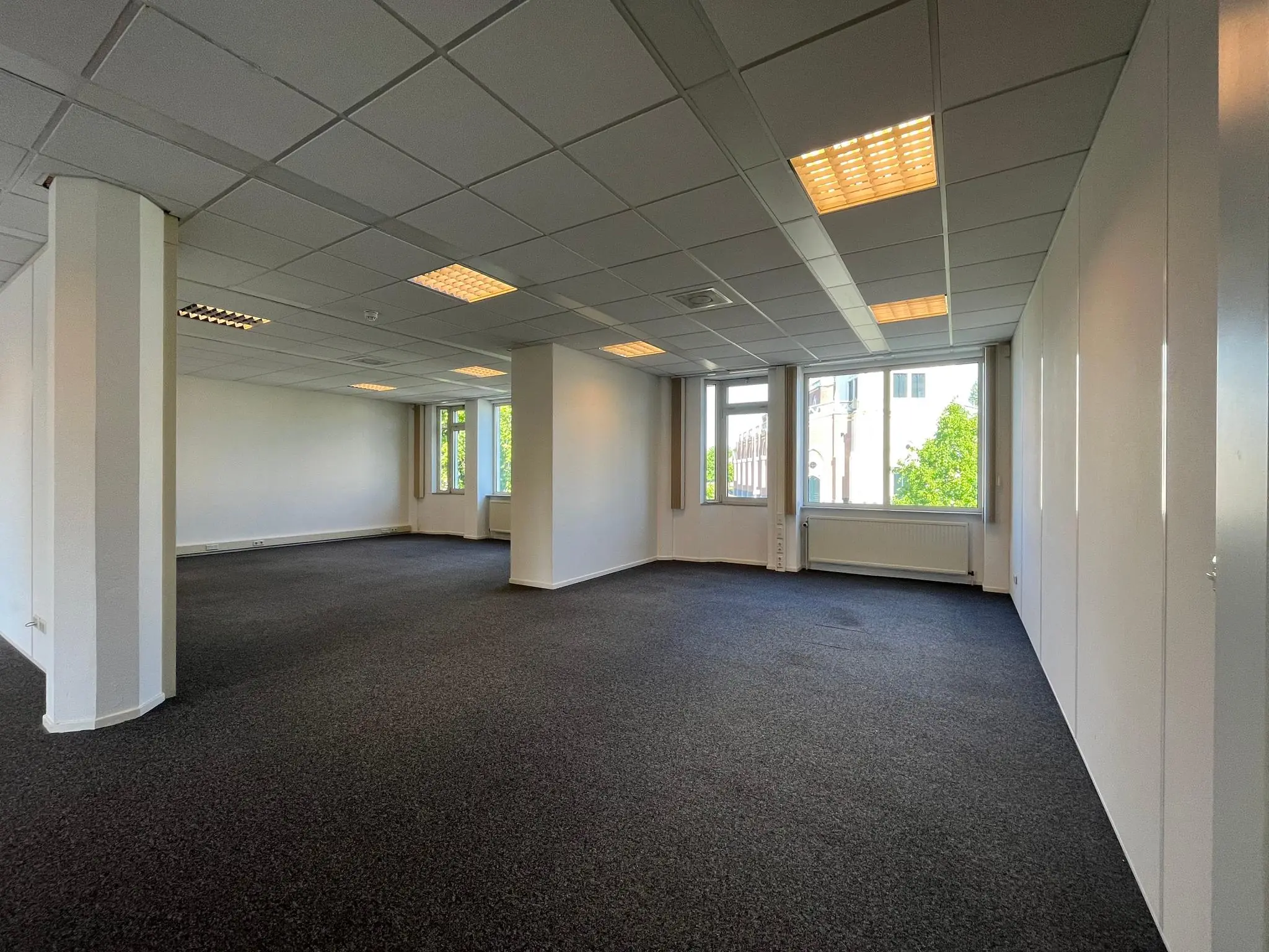 Leeg, licht kantoorpand aan de Utrechtseweg met systeemplafond en grote ramen.