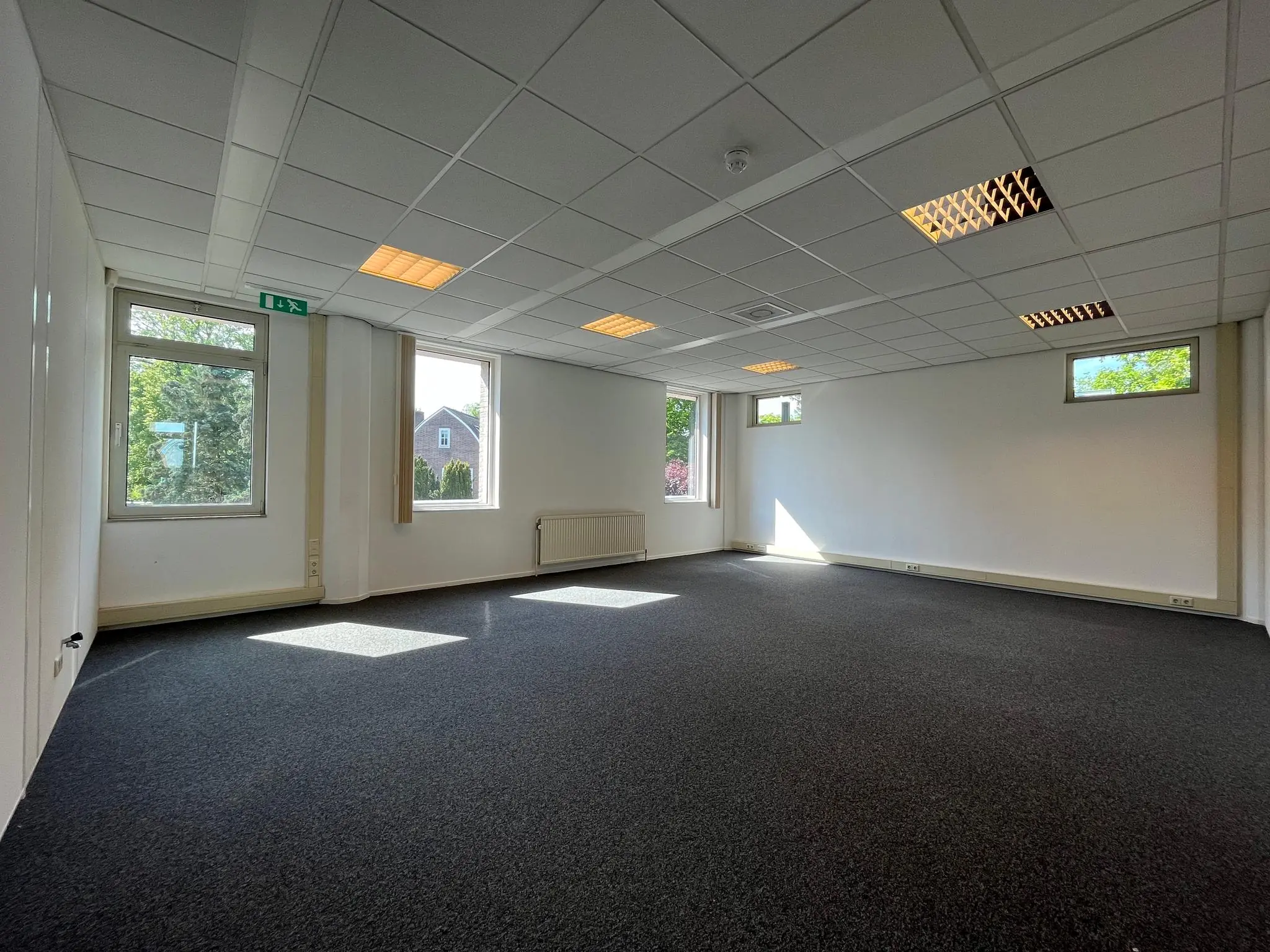 Lichte, lege kantoorruimte aan de Utrechtseweg met systeemplafond, grijze vloerbedekking en meerdere ramen.