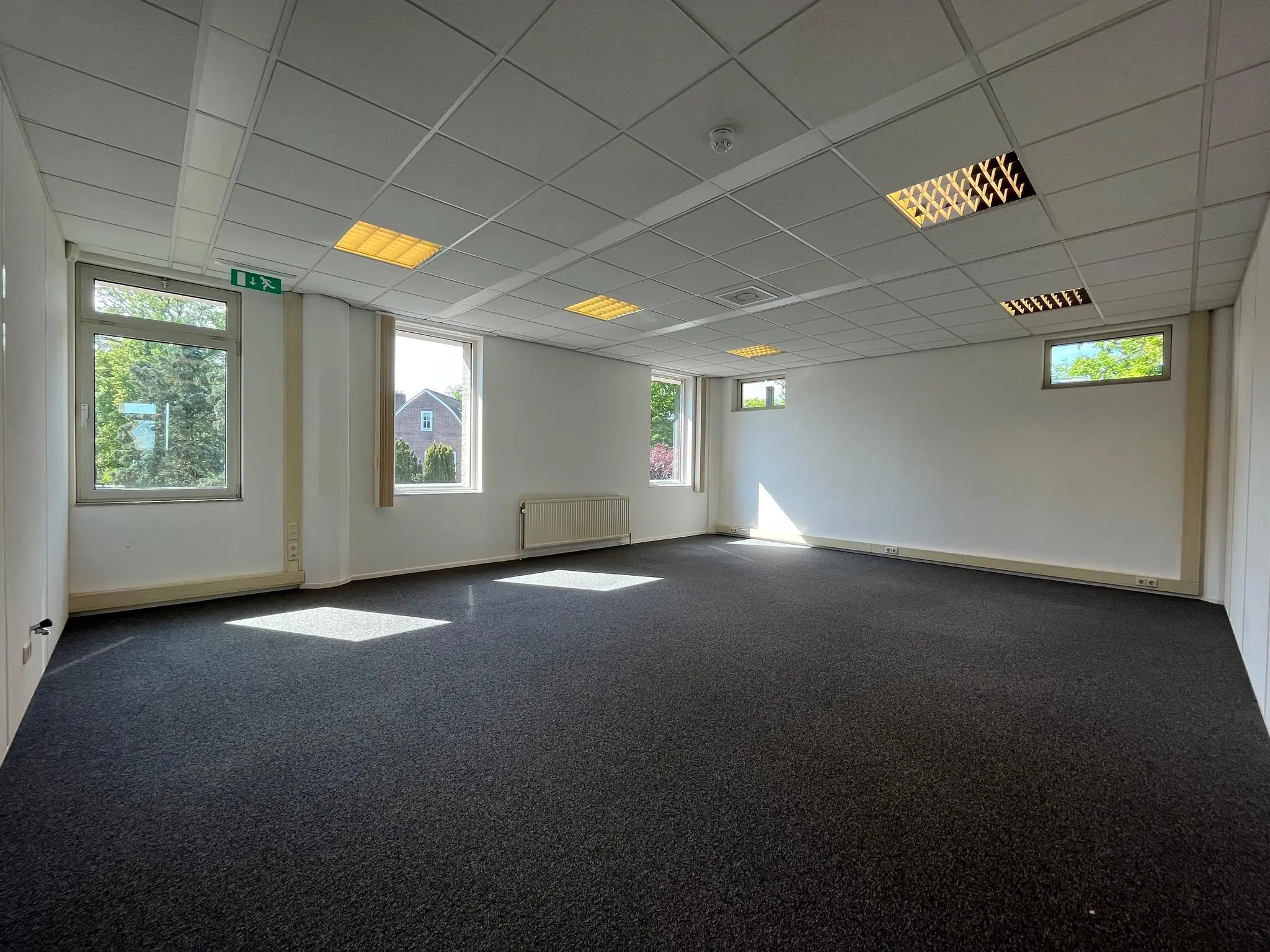 Lichte, lege kantoorruimte aan de Utrechtseweg met systeemplafond, tapijtvloer en meerdere ramen.