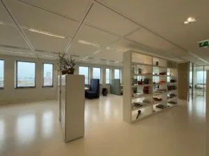 Modern kantoorinterieur op het IJdok met grote ramen, open werkplekken en een open boekenkast als ruimteverdeler.