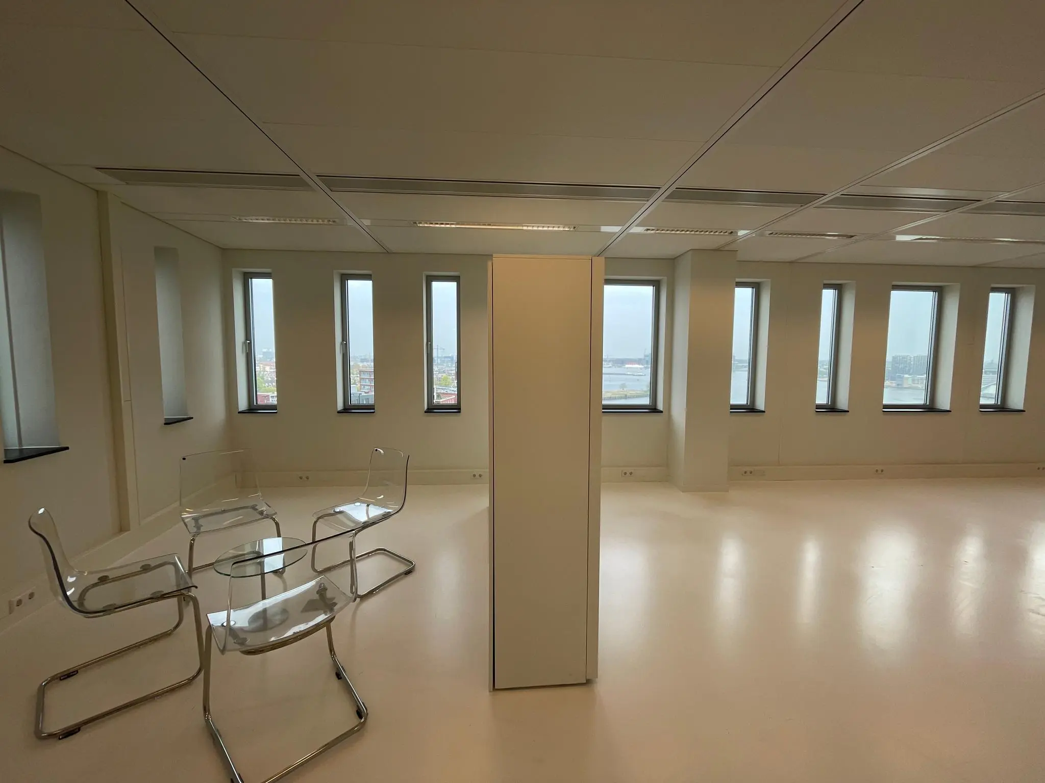 Licht, leeg kantoorpand aan het IJdok met glazen stoelen en tafel bij de ramen.