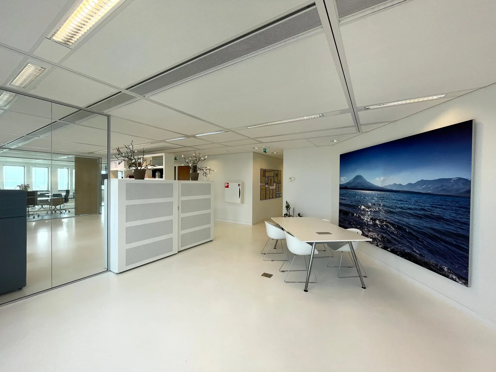 Moderne en lichte kantoorruimte met vergadertafel, witte stoelen en een grote wandfoto van de IJDok-haven met bergachtig landschap.