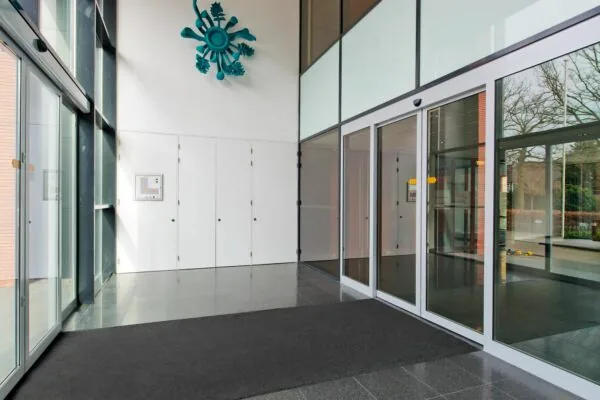 Ingang van een modern kantoorgebouw aan de Groenekanseweg met glazen schuifdeuren, witte kasten en een opvallend blauw kunstwerk aan de muur.