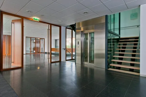 Moderne kantoorhal aan de Groenekanseweg met glazen deuren, lift en een open trap.