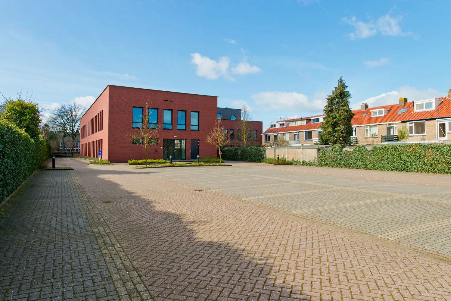 Modern rood bakstenen kantoorpand aan de Groenekanseweg met een leeg parkeerterrein op de voorgrond.