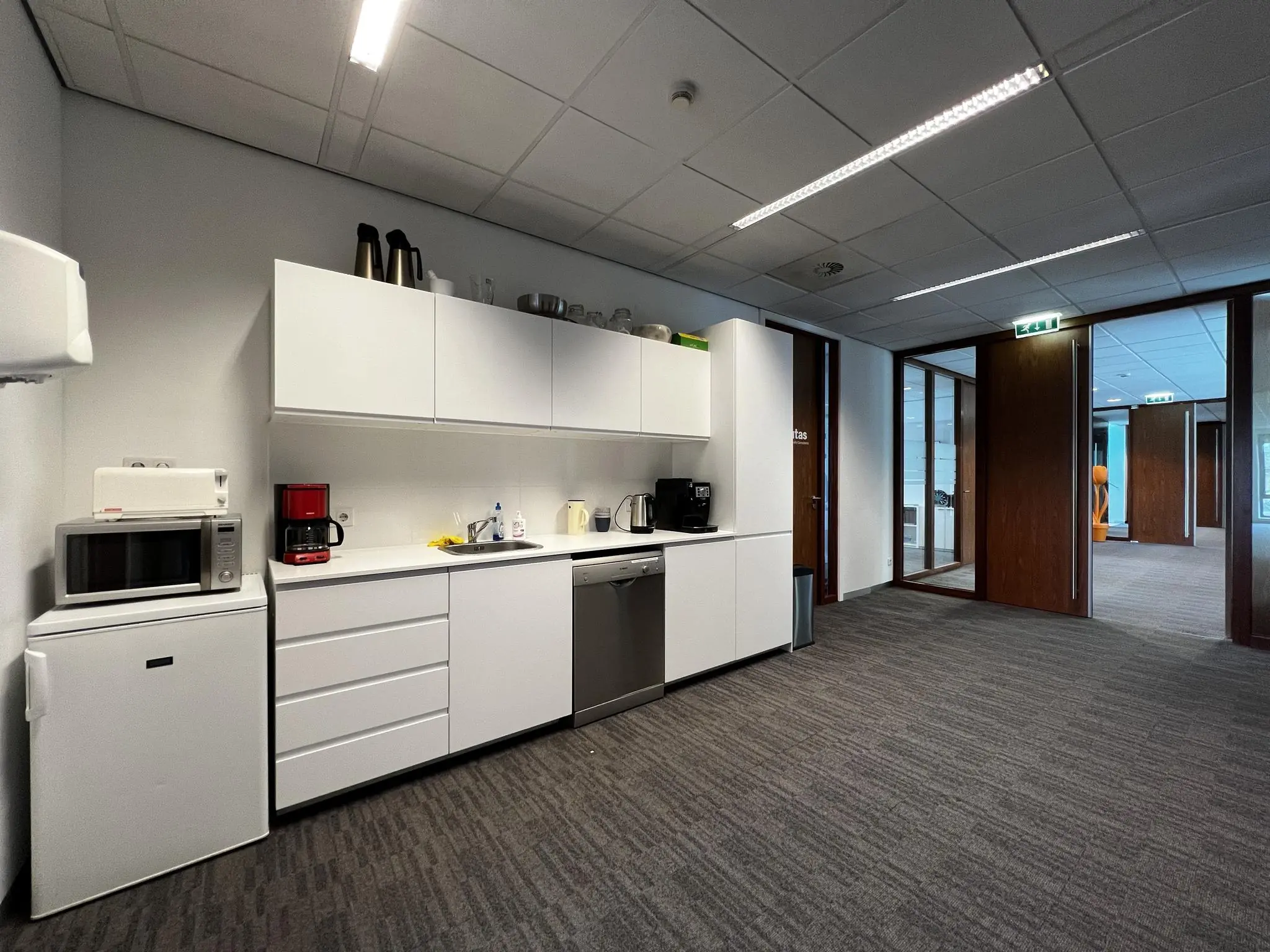 Kleine pantry met witte keukenopstelling in een modern kantoorgebouw aan de Groenekanseweg.