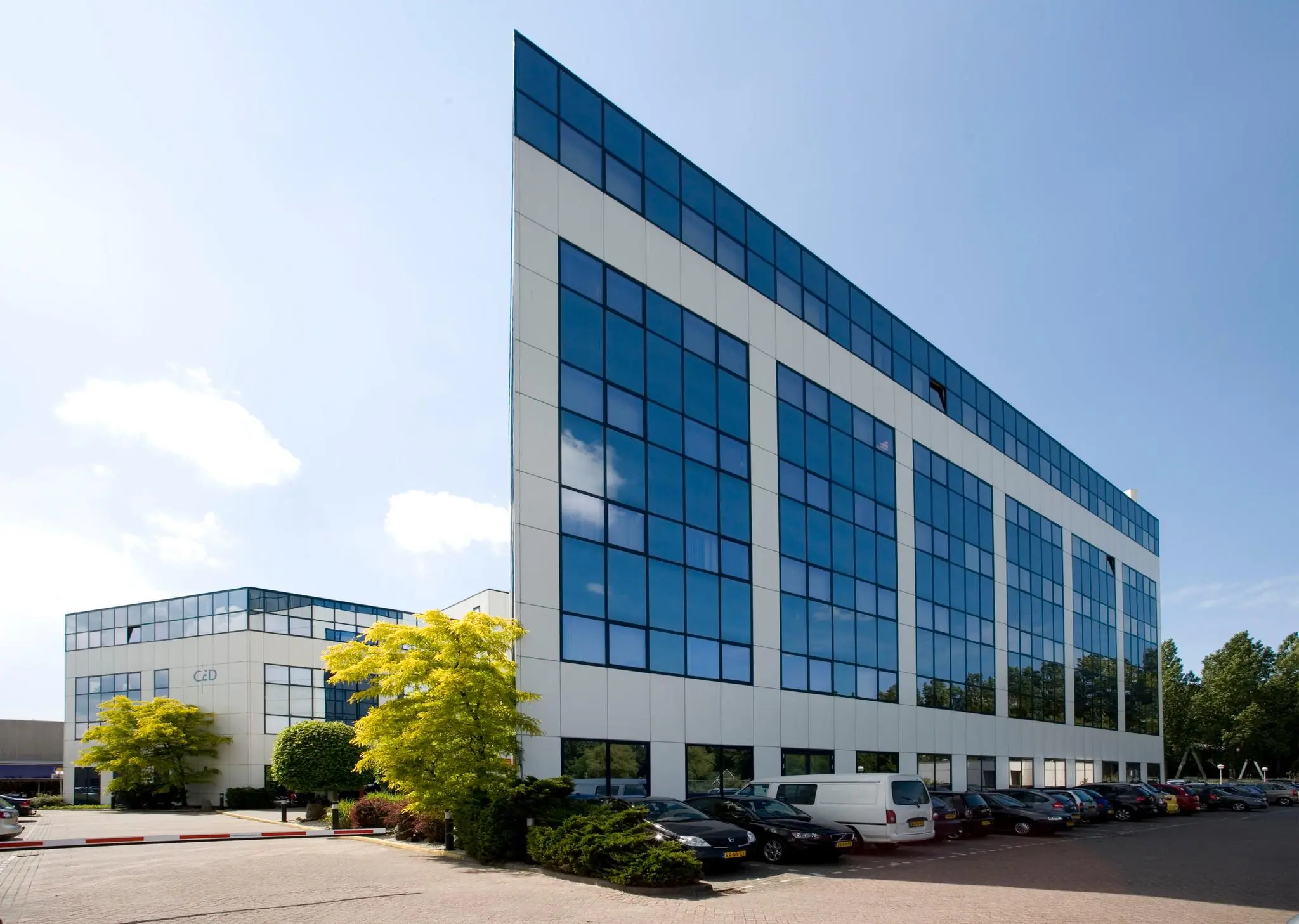 Modern kantoorgebouw aan de Rietbaan met spiegelende ramen en een parkeerterrein aan de voorzijde.