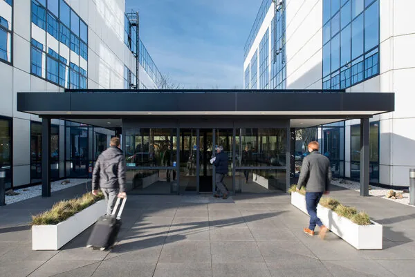 Personen lopen een modern kantoorgebouw aan de Rietbaan binnen via een glazen entree.