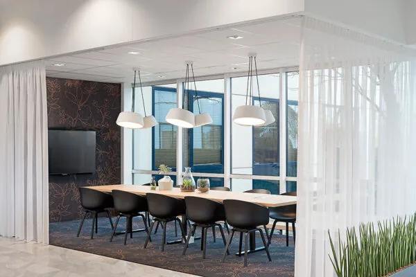 Vergaderruimte aan de Rietbaan met een lange tafel, zwarte stoelen, hanglampen en grote ramen met uitzicht naar buiten.