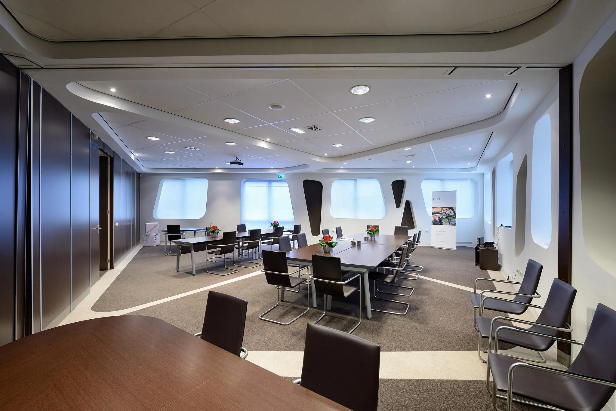 Moderne vergaderruimte aan de Rietbaan met grote ramen, strakke inrichting en meerdere vergadertafels met stoelen.
