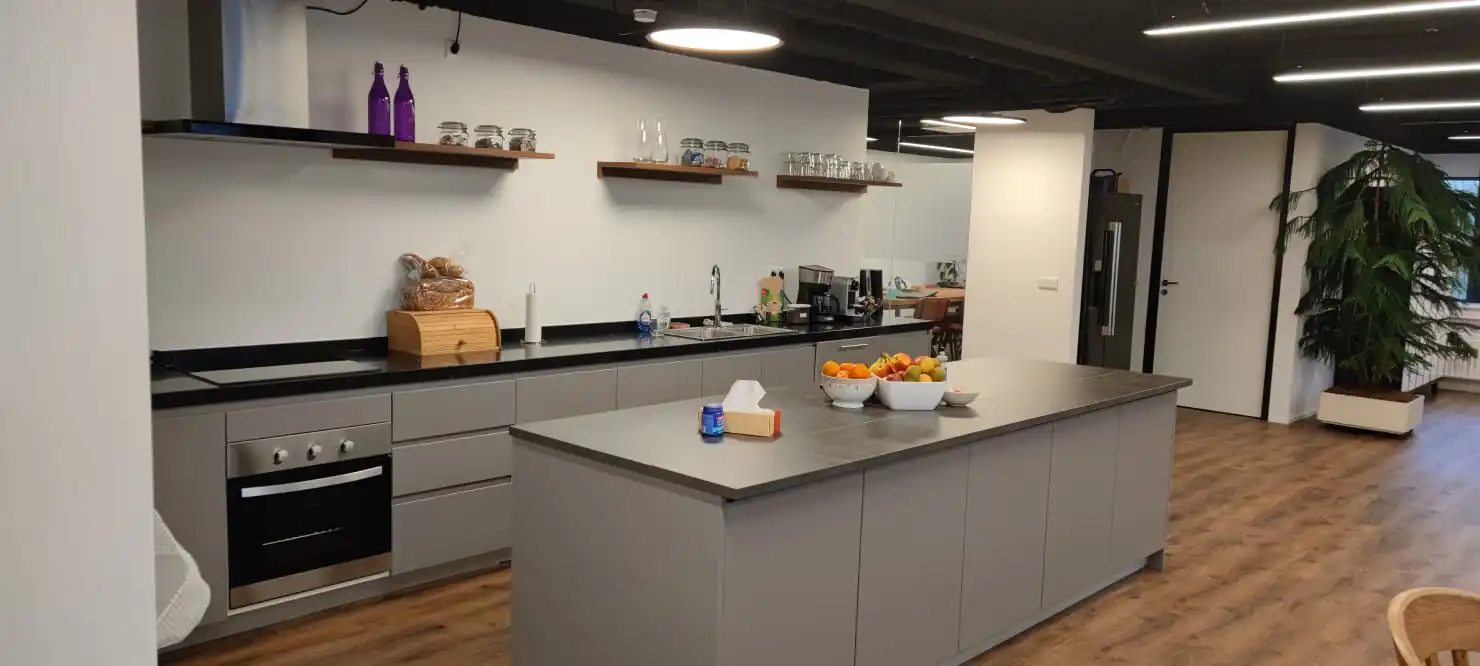 Moderne kantoorkeuken aan de Rietbaan met grijze kasten, een kookeiland en open houten wandplanken.