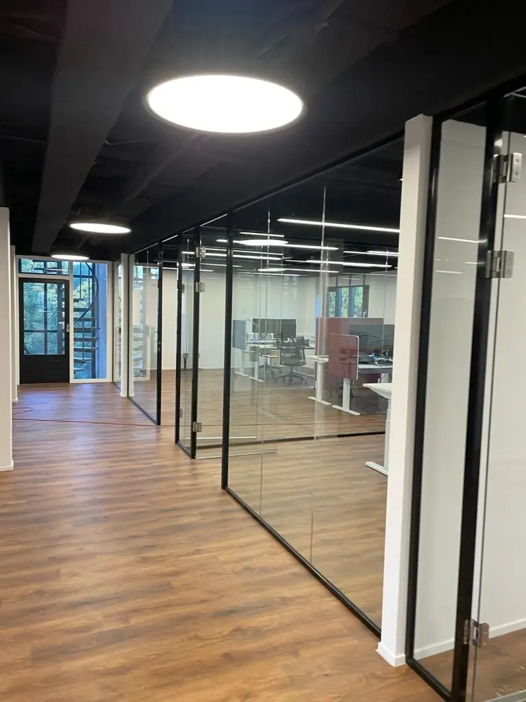 Moderne kantoorruimte aan de Rietbaan met glazen wanden, houten vloer en zicht op werkplekken.