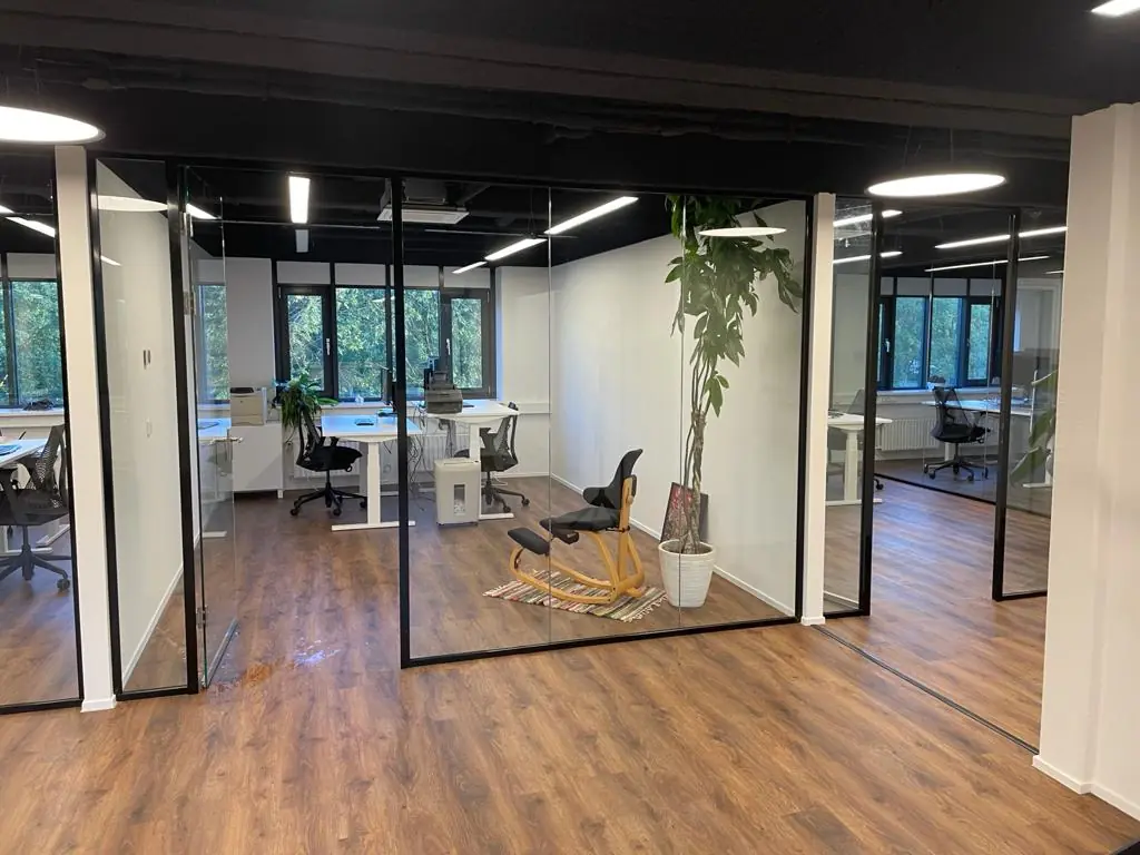 Modern kantoorinterieur aan de Rietbaan met glazen wanden, houten vloer en werkplekken bij grote ramen.