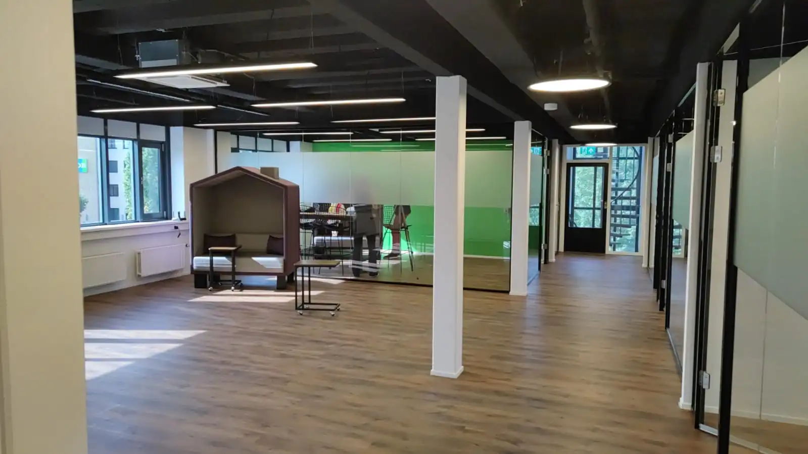 Modern kantoorinterieur aan de Rietbaan met glazen vergaderruimtes, houten vloer en een zithoek met akoestische bank.