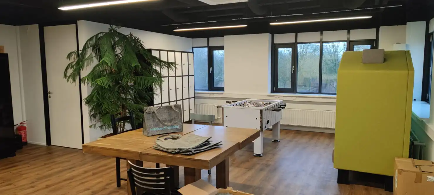 Moderne kantoorruimte aan de Rietbaan met een tafel, lockers, een tafelvoetbaltafel en een groene zitunit.