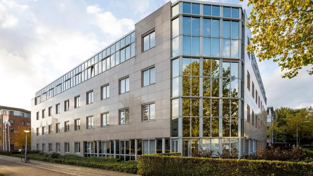 Modern kantoorgebouw met veel glaspartijen, genaamd Wisselwerking, op een zonnige herfstdag.