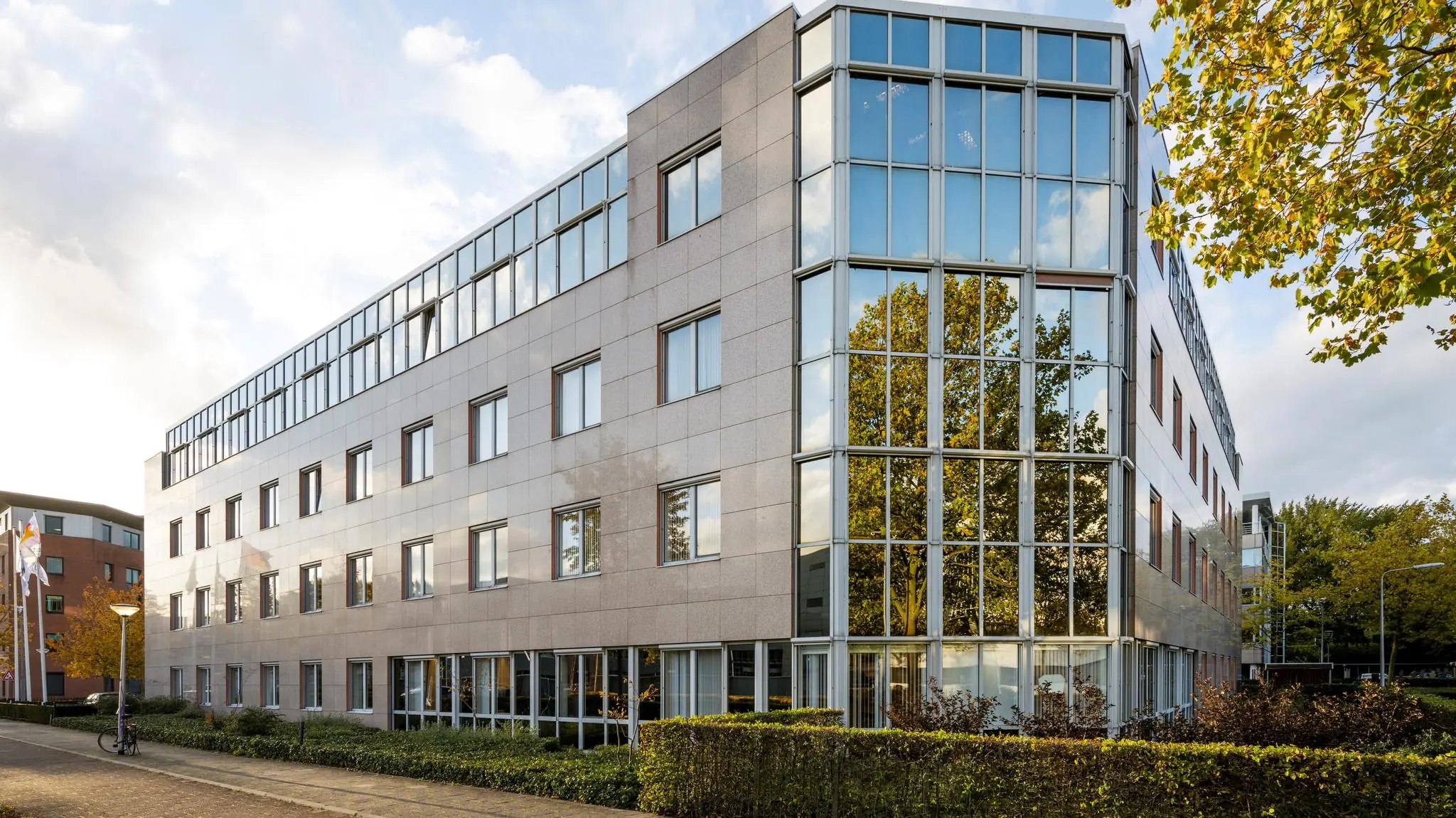 Modern kantoorgebouw met veel glaspartijen, genaamd Wisselwerking, op een zonnige herfstdag.