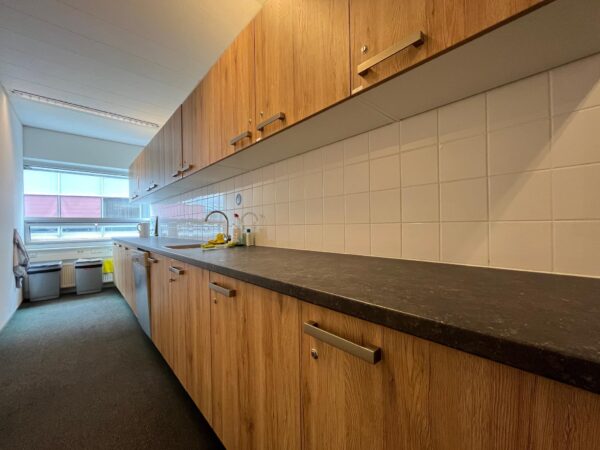 Keuken met houten kastjes, zwart aanrechtblad en witte tegelwand in een kantoor aan de Arnhemseweg.