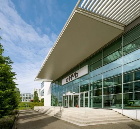 Vooraanzicht van het moderne kantoorgebouw d'Hub aan de Capellalaan, met glazen gevel en overstekend dak.