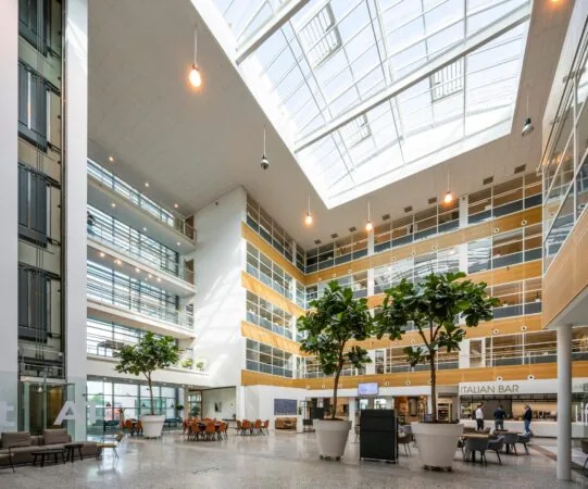 Lichte en moderne kantoorlobby aan de Capellalaan met hoge glazen dakramen, zitplekken en een Italian Bar.