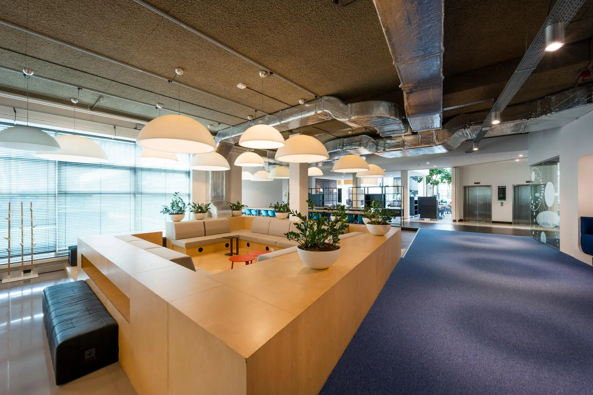 Moderne en ruime kantoorlounge aan de Capellalaan met zithoek, grote hanglampen en plantenbakken.