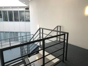 Trappenhuis met metalen leuning in een kantoorgebouw aan de Zekeringstraat, met zicht op kantoren achter glazen ramen.