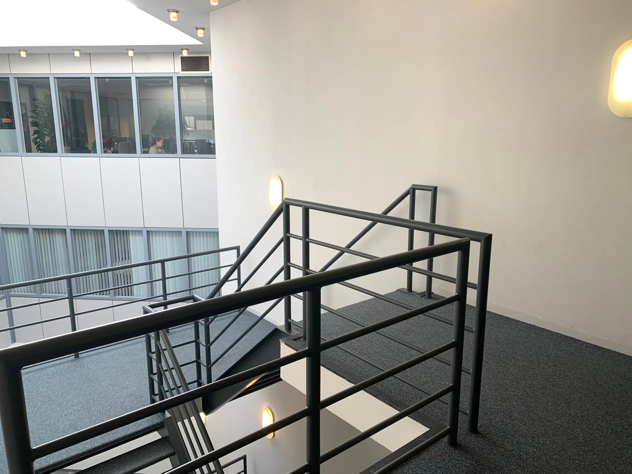 Trappenhuis met metalen leuning in een kantoorgebouw aan de Zekeringstraat, met zicht op kantoren achter glazen ramen.