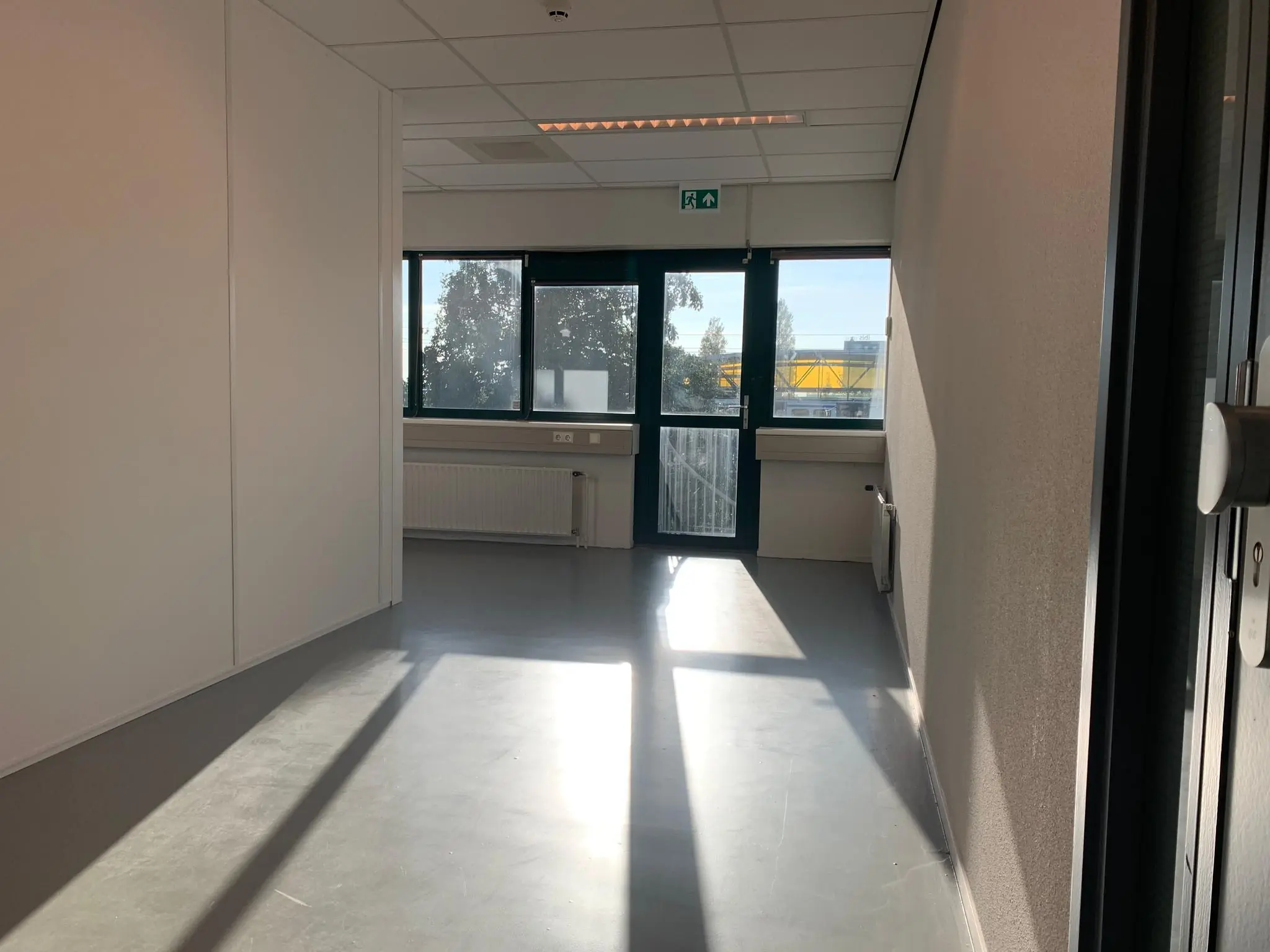 Lichte kantoorruimte aan de Zekeringstraat met grote ramen en grijze vloer.