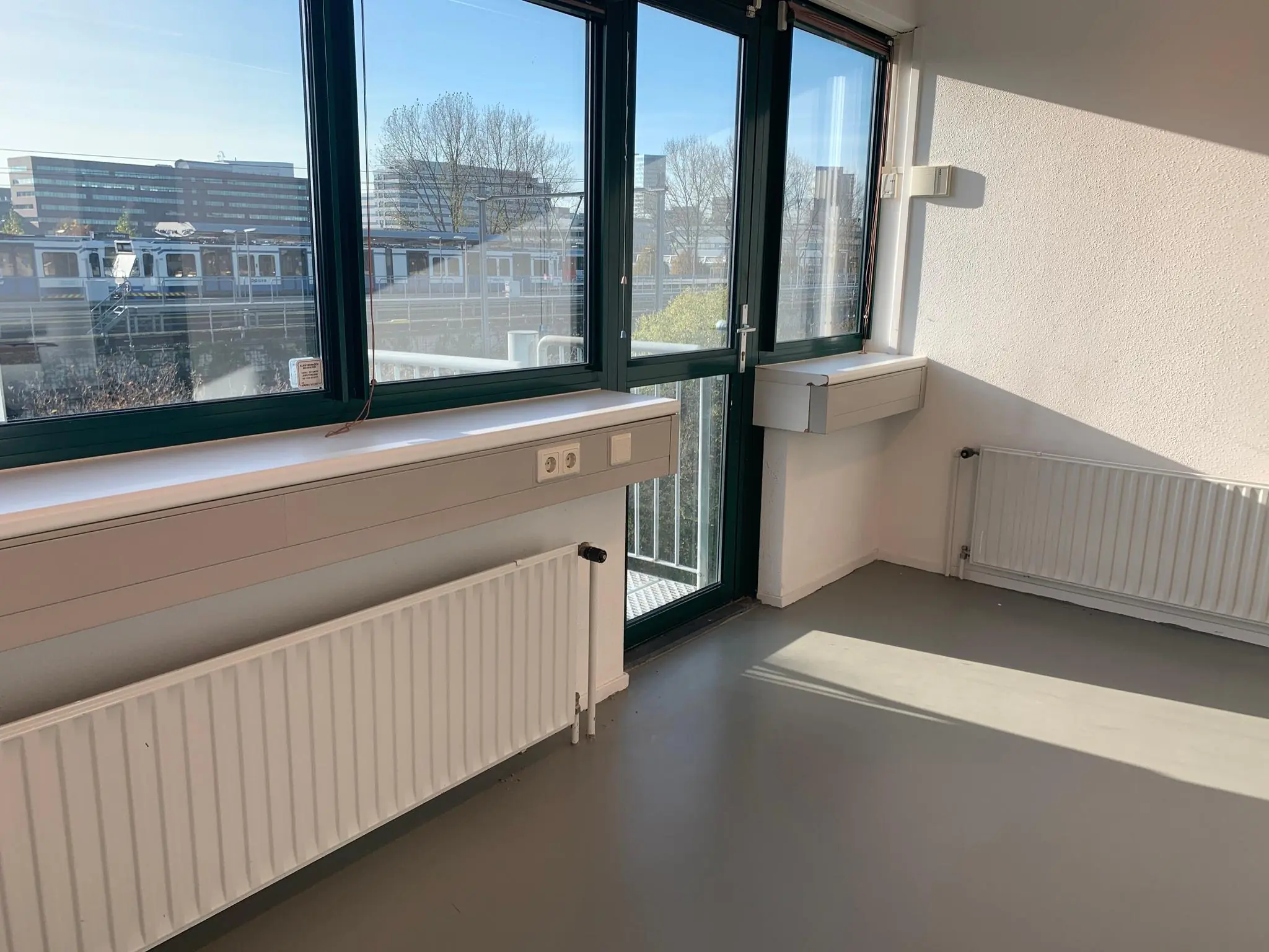 Leeg en licht kantoorruimte met grote ramen en uitzicht op een metrostation aan de Zekeringstraat.