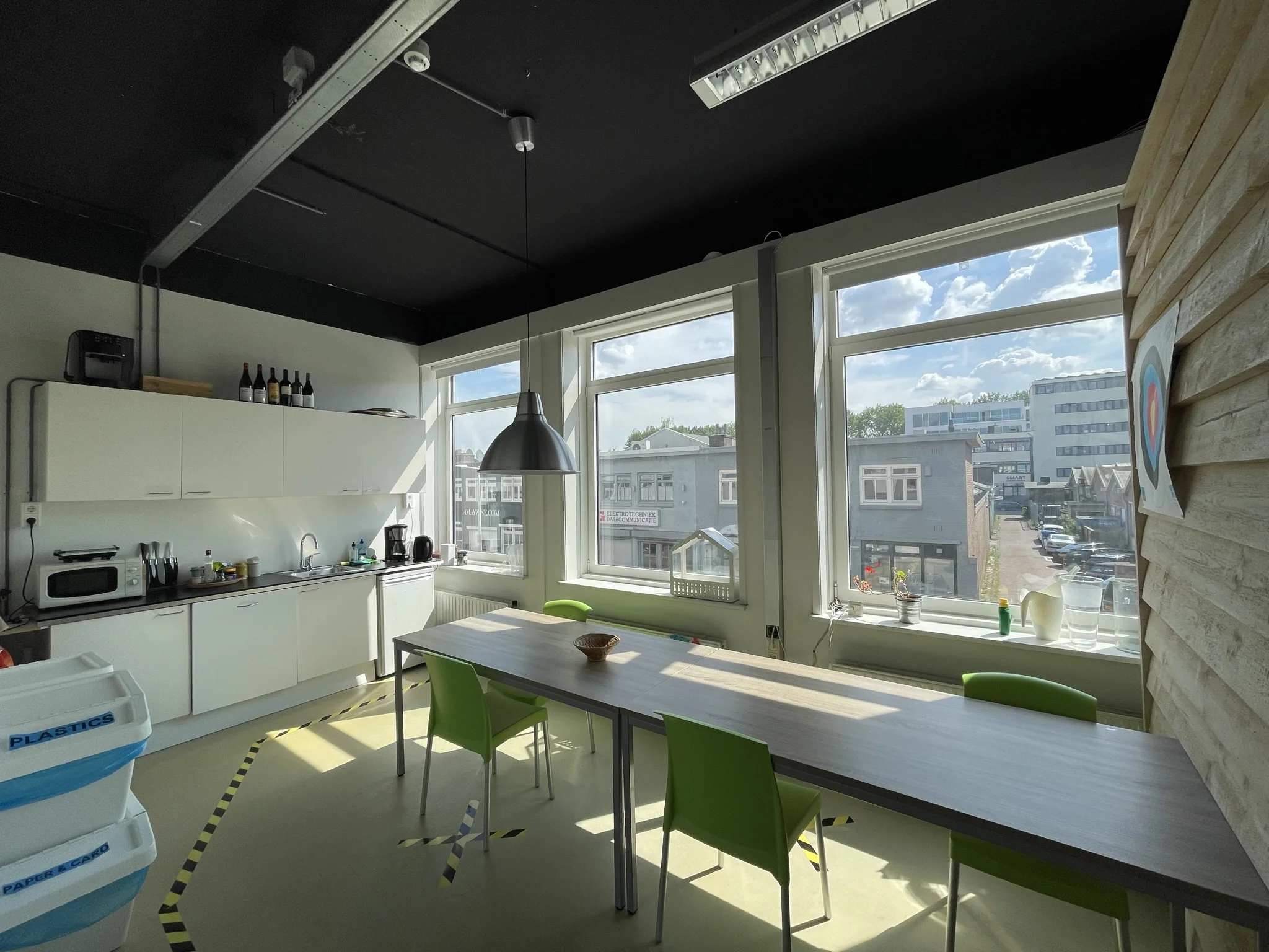 Kleine kantoorkeuken met een lange tafel en uitzicht op bedrijventerrein aan de Pilotenstraat.