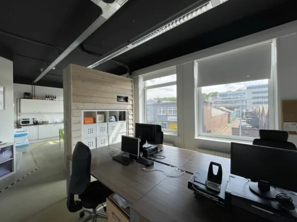 Kantoorruimte aan de Pilotenstraat met bureaus, computers, een keukentje en uitzicht op een bedrijventerrein.