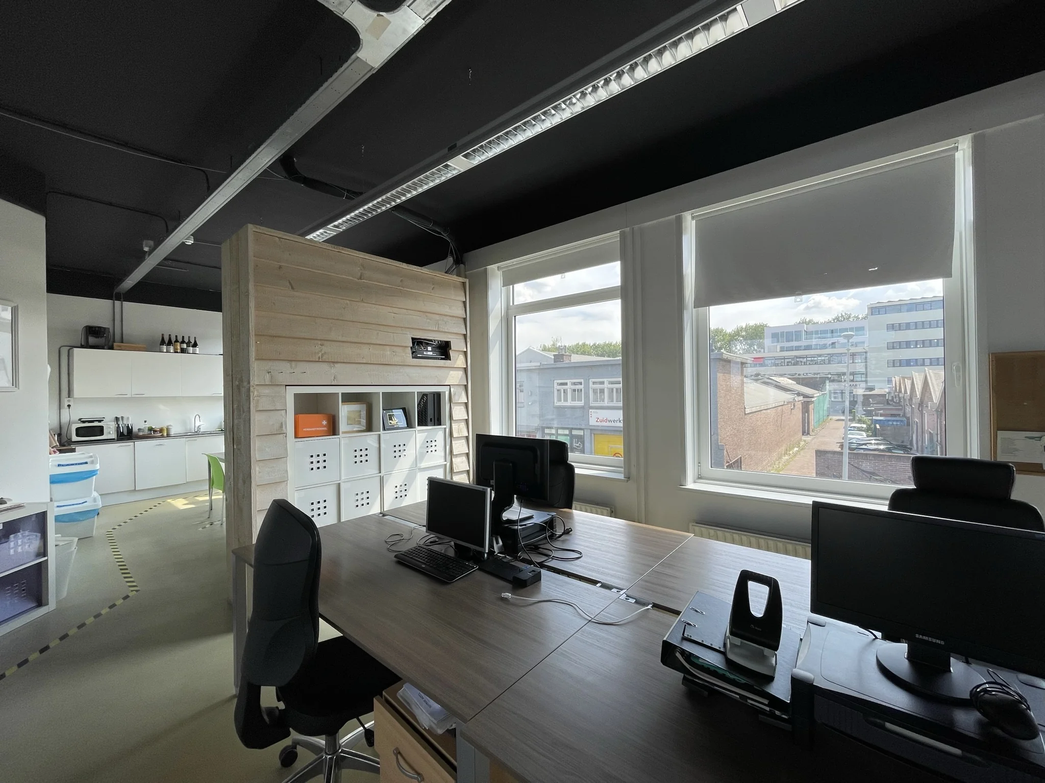 Kantoorruimte aan de Pilotenstraat met bureaus, computers, een keukentje en uitzicht op een bedrijventerrein.
