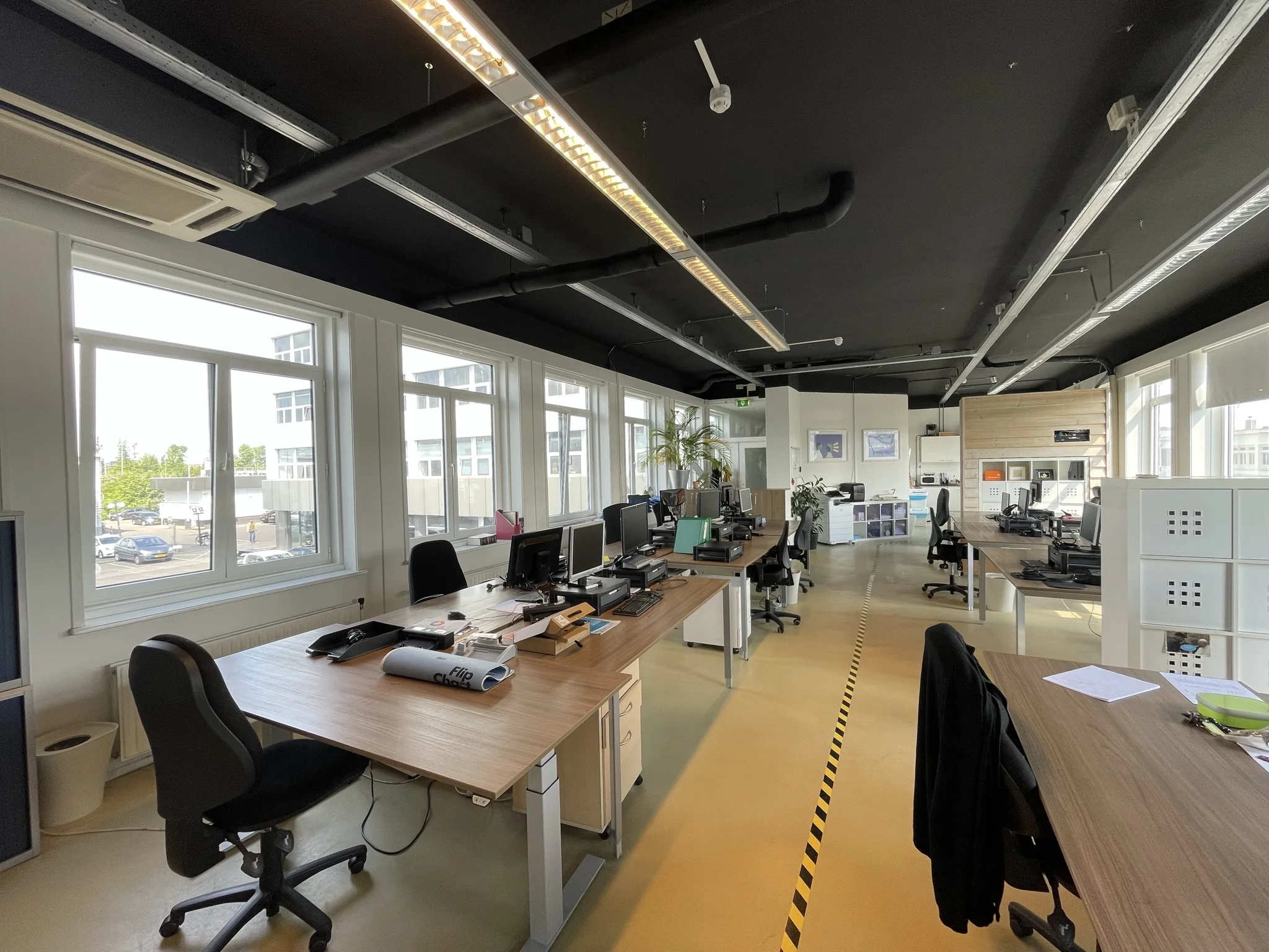 Modern kantoorpand aan de Pilotenstraat met meerdere bureaus, computers en grote ramen die veel daglicht binnenlaten.