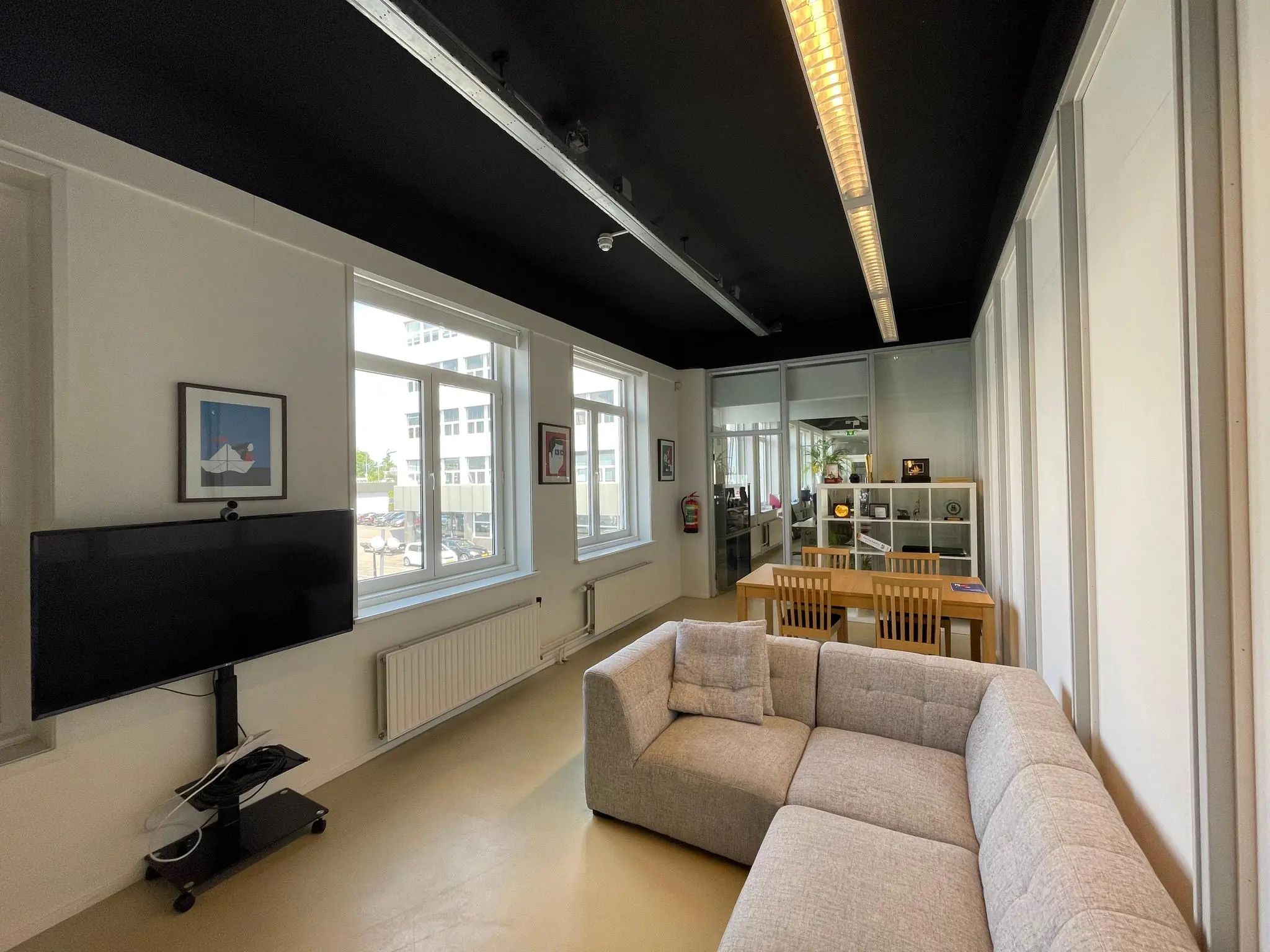 Modern ingerichte kantoorruimte aan de Pilotenstraat met een grijze hoekbank, grote ramen, vergadertafel en flatscreen-tv.