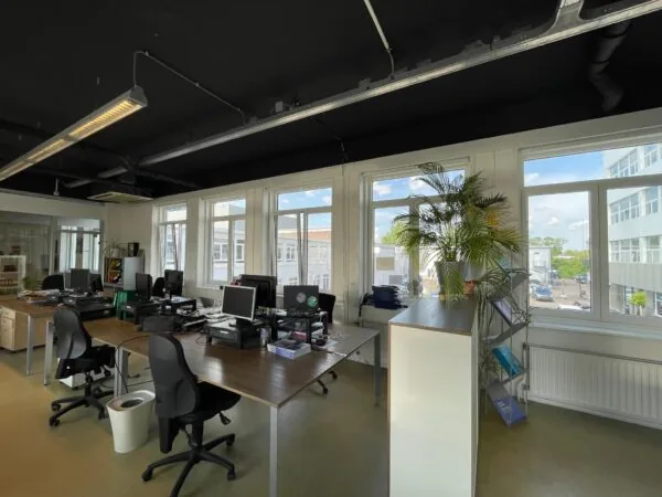 Modern kantoorruimte aan de Pilotenstraat met meerdere bureaus, computers en grote ramen met uitzicht op omliggende gebouwen.