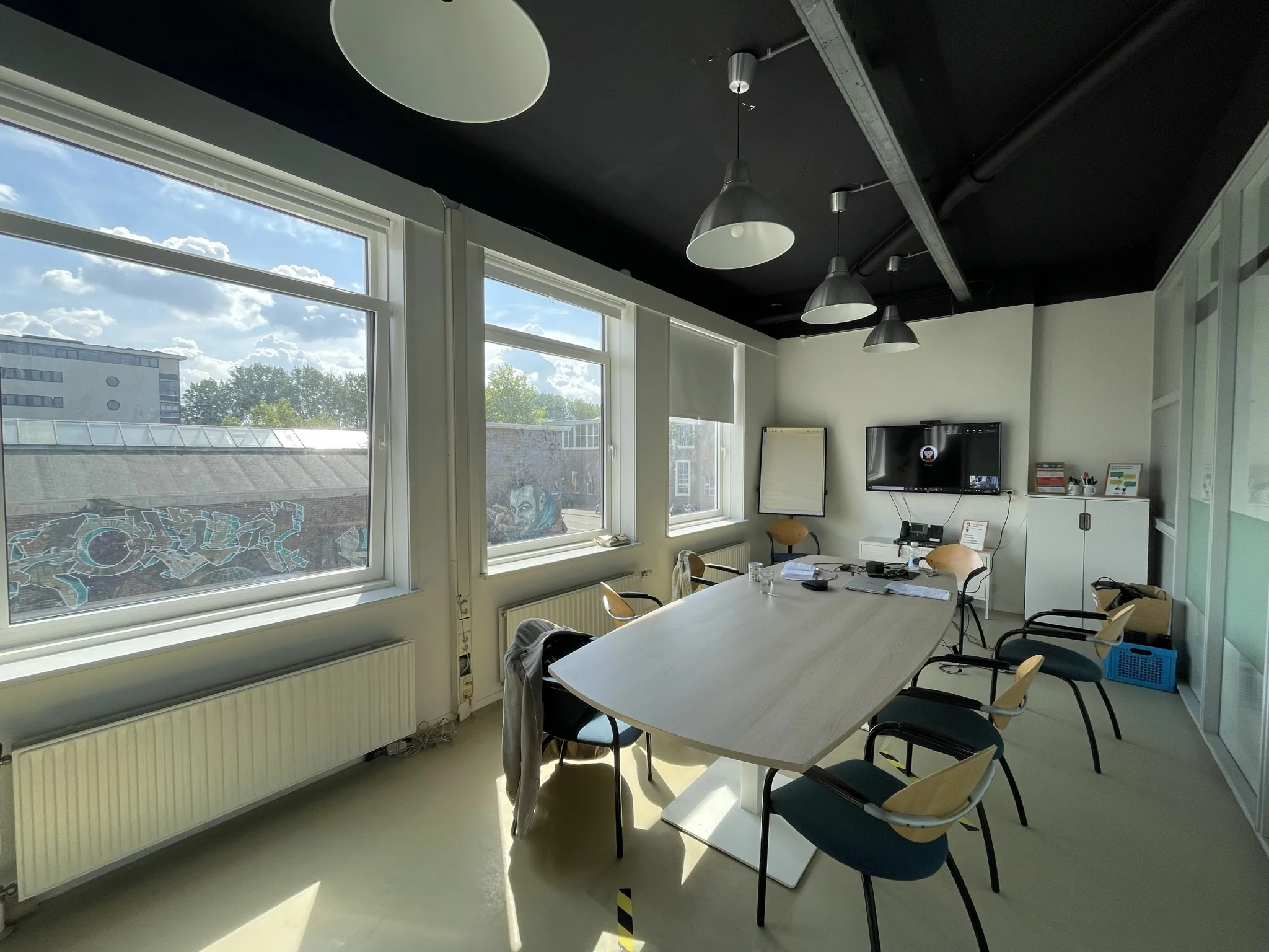 Vergaderruimte op de Pilotenstraat met grote ramen, een lange tafel, stoelen en een scherm aan de muur.