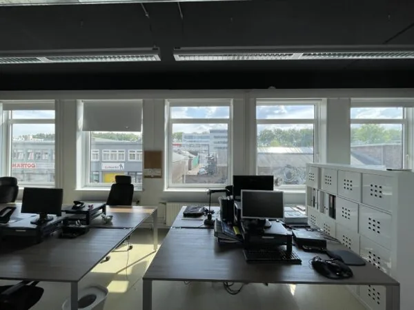 Open kantoorruimte met meerdere bureaus en computers, met uitzicht op bedrijfsgebouwen aan de Pilotenstraat in Amsterdam.