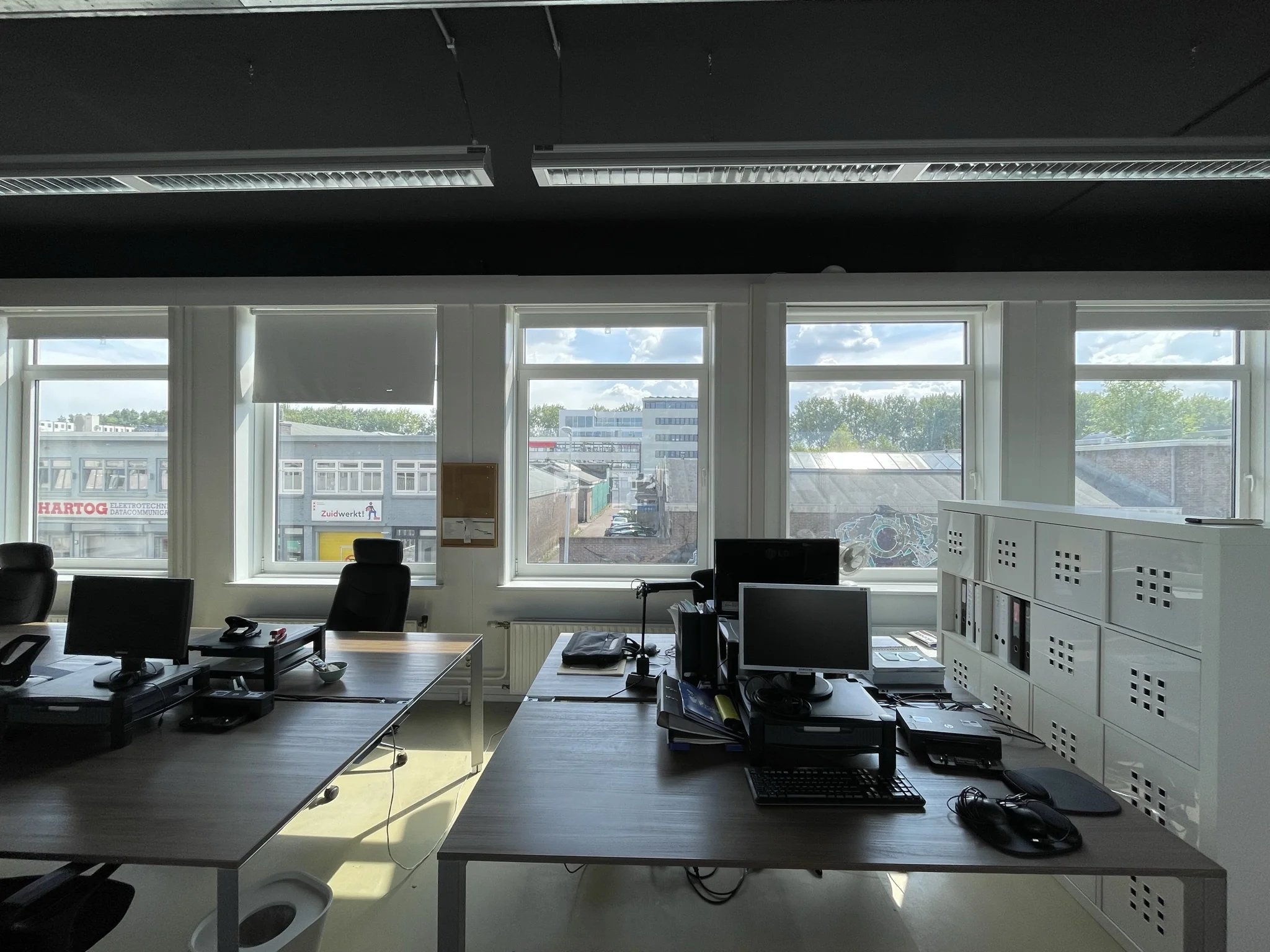 Open kantoorruimte met meerdere bureaus en computers, met uitzicht op bedrijfsgebouwen aan de Pilotenstraat in Amsterdam.