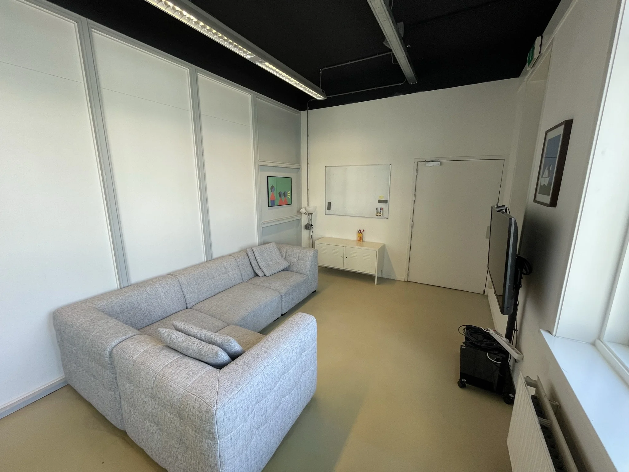 Moderne vergaderruimte op de Pilotenstraat met grijze hoekbank, wanddecoratie, whiteboard en tv-scherm.