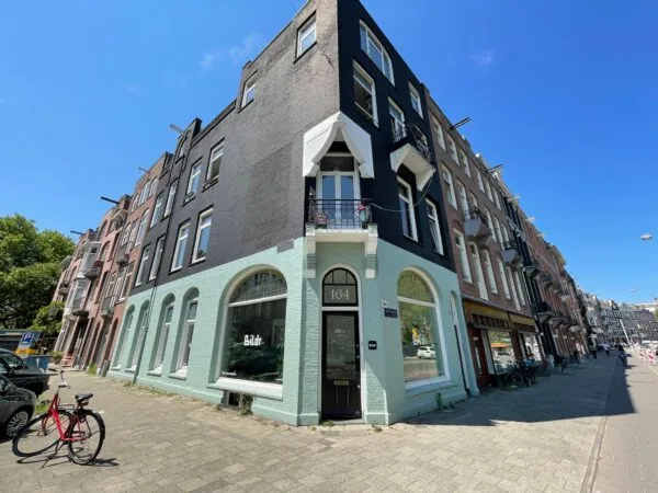 Hoekpand aan de Nassaukade met zwart-mintgroene gevel en het pandnummer 164, op een zonnige dag.