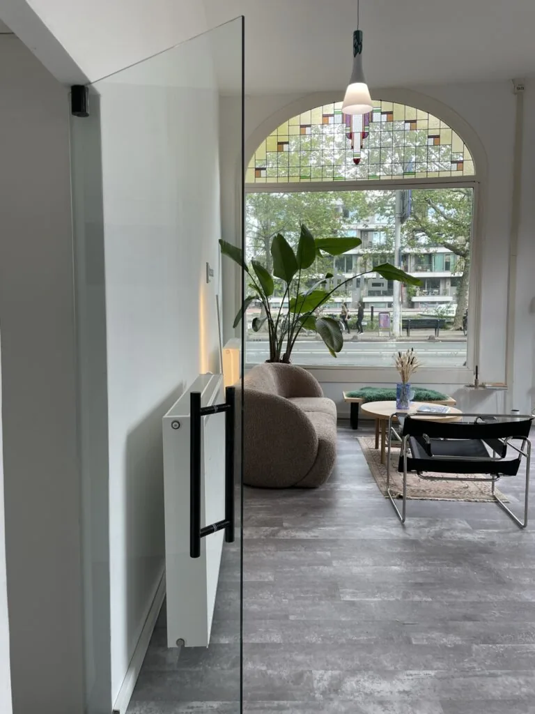 Modern ingerichte woonkamer aan de Nassaukade met een groot raam met glas-in-lood en uitzicht op de straat.