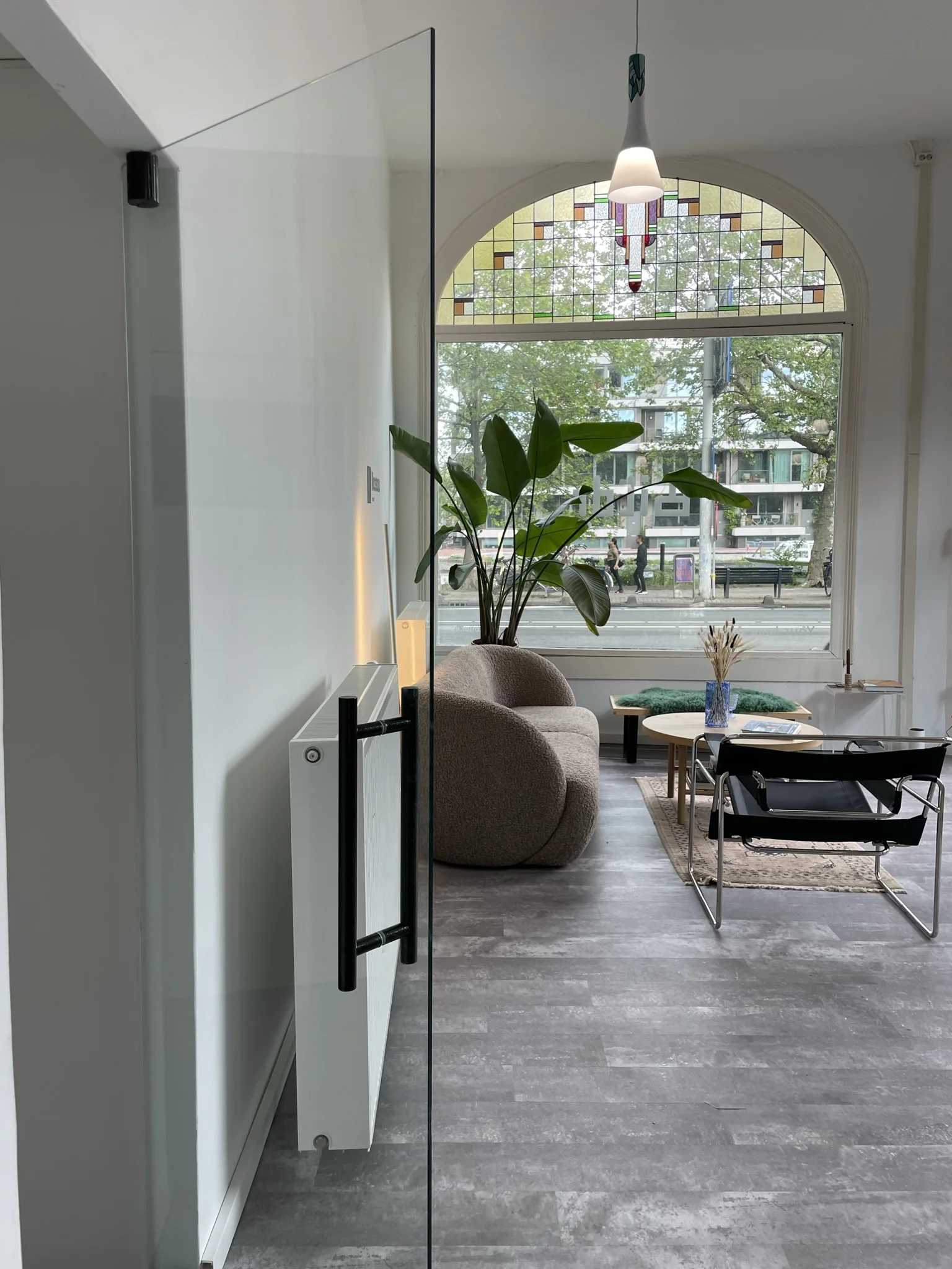 Modern ingerichte woonkamer aan de Nassaukade met een groot raam met glas-in-lood en uitzicht op de straat.