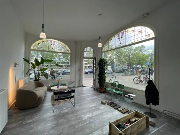 Lichte en modern ingerichte ruimte aan de Nassaukade met grote ramen, houten vloerstaaltjes en uitzicht op een drukke straat met fietsen en auto's.