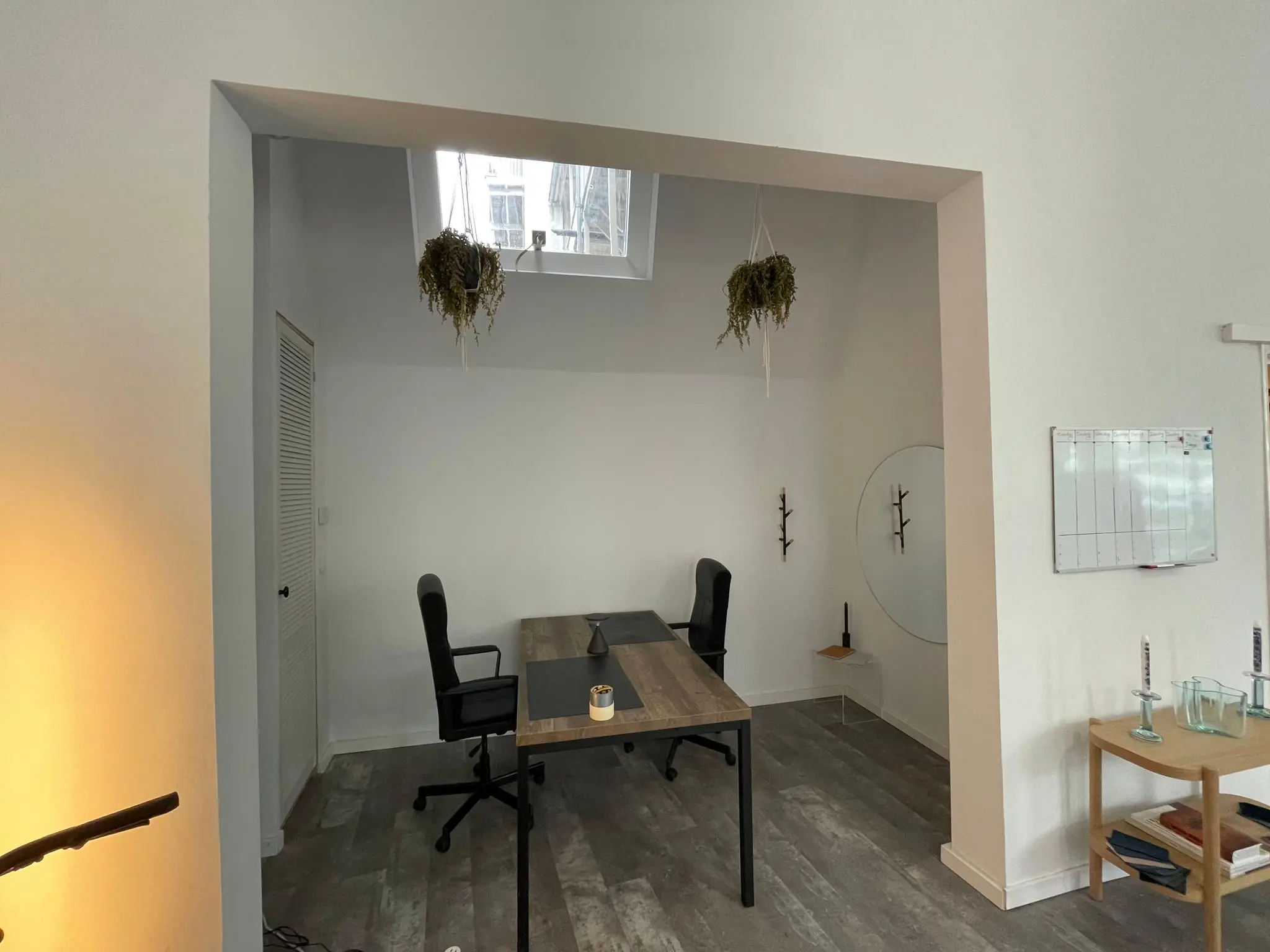 Twee moderne bureaus met bureaustoelen in een minimalistisch ingericht kantoor aan de Nassaukade, met hangplanten en een glazen whiteboard.