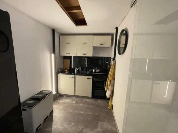 Kleine keuken aan de Nassaukade met beige kastjes, zwarte apparatuur en een plafondopening.