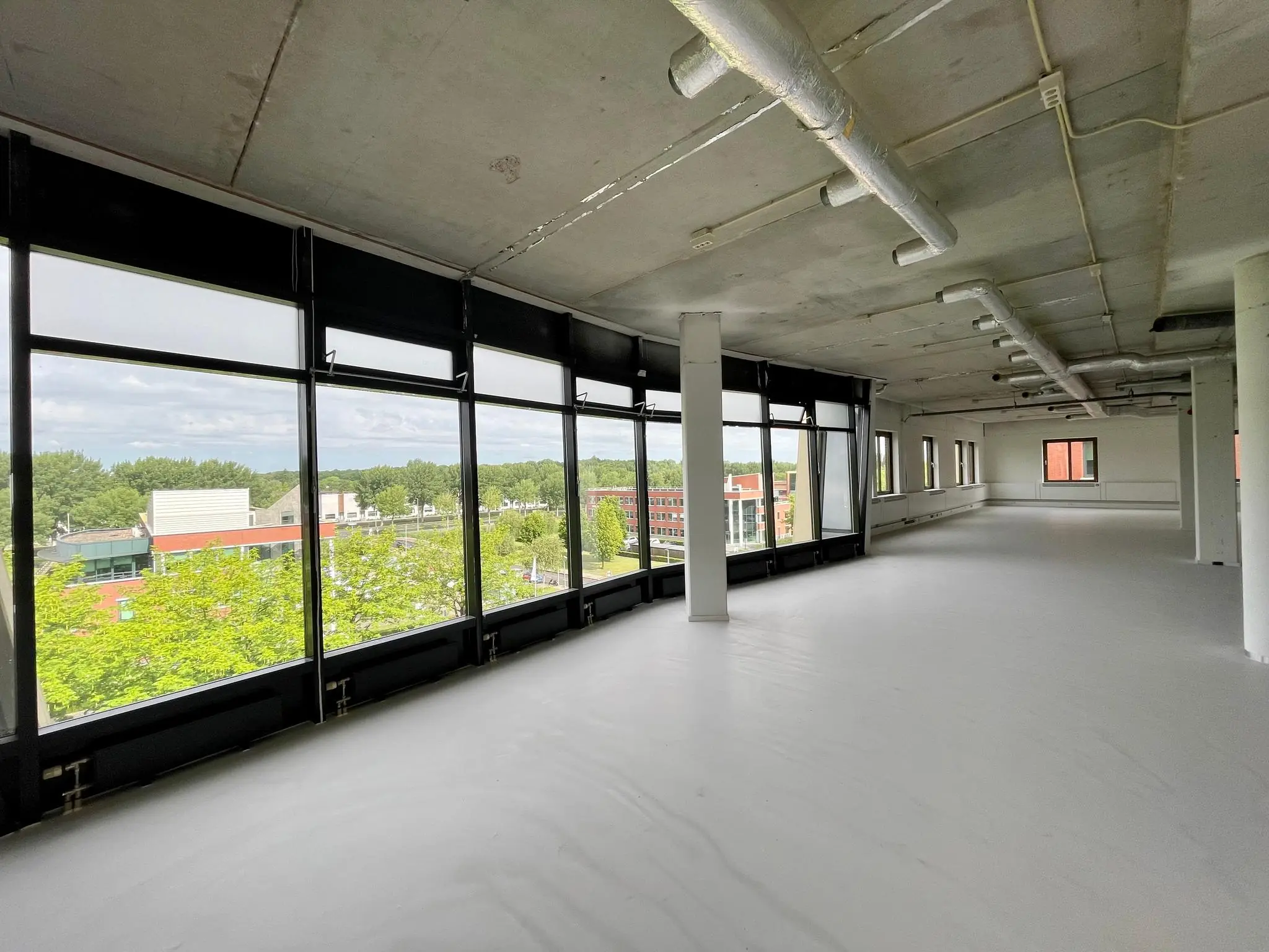 Licht en ruim leeg kantoorpand aan de Lichtenauerlaan met grote ramen en uitzicht op groen en omliggende gebouwen.