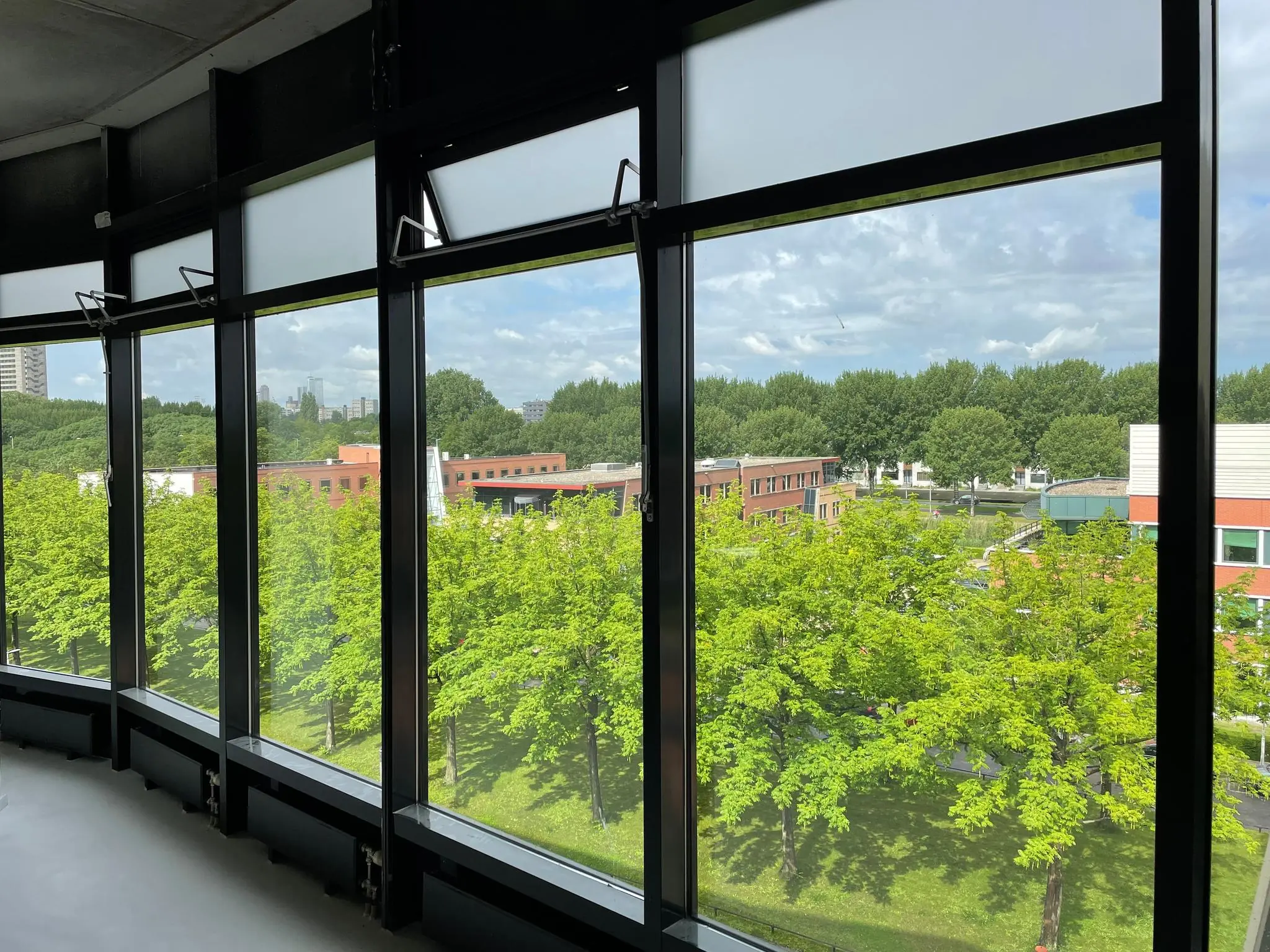 Uitzicht vanuit een hoog gebouw aan de Lichtenauerlaan op een groene wijk met bomen en kantoorpanden.