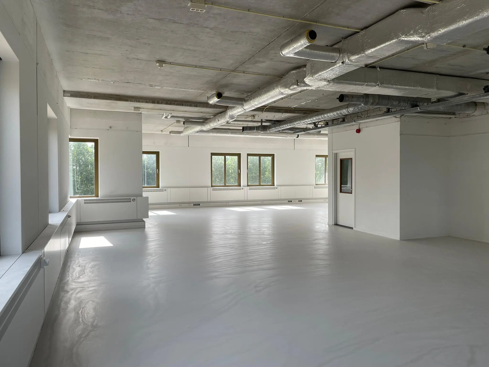 Lichte, lege kantoorruimte aan de Lichtenauerlaan met witte vloeren, zichtbare plafondinstallaties en grote ramen.