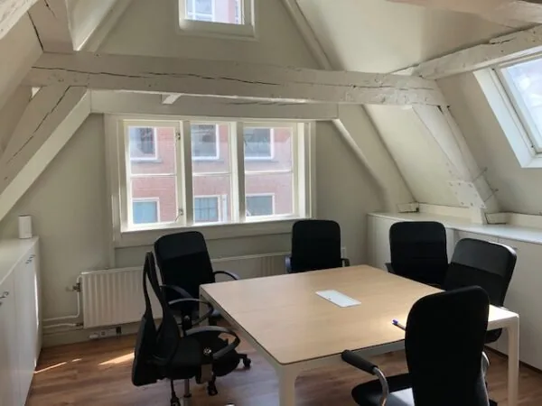 Vergaderruimte met vijf zwarte stoelen rond een houten tafel in een lichte zolderkamer aan de Herengracht.