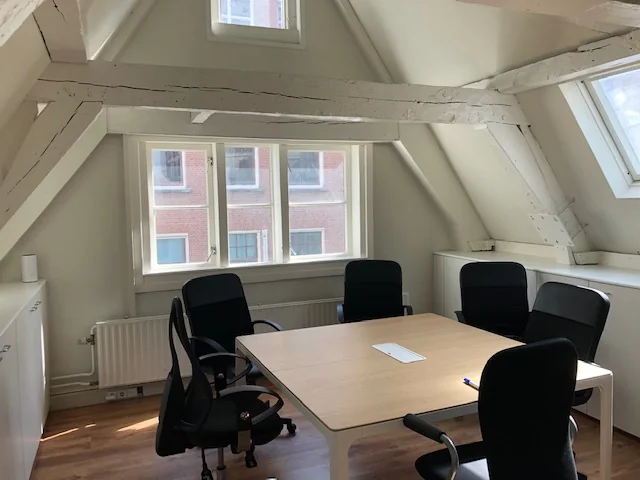 Vergaderruimte met vijf zwarte stoelen rond een houten tafel in een lichte zolderkamer aan de Herengracht.